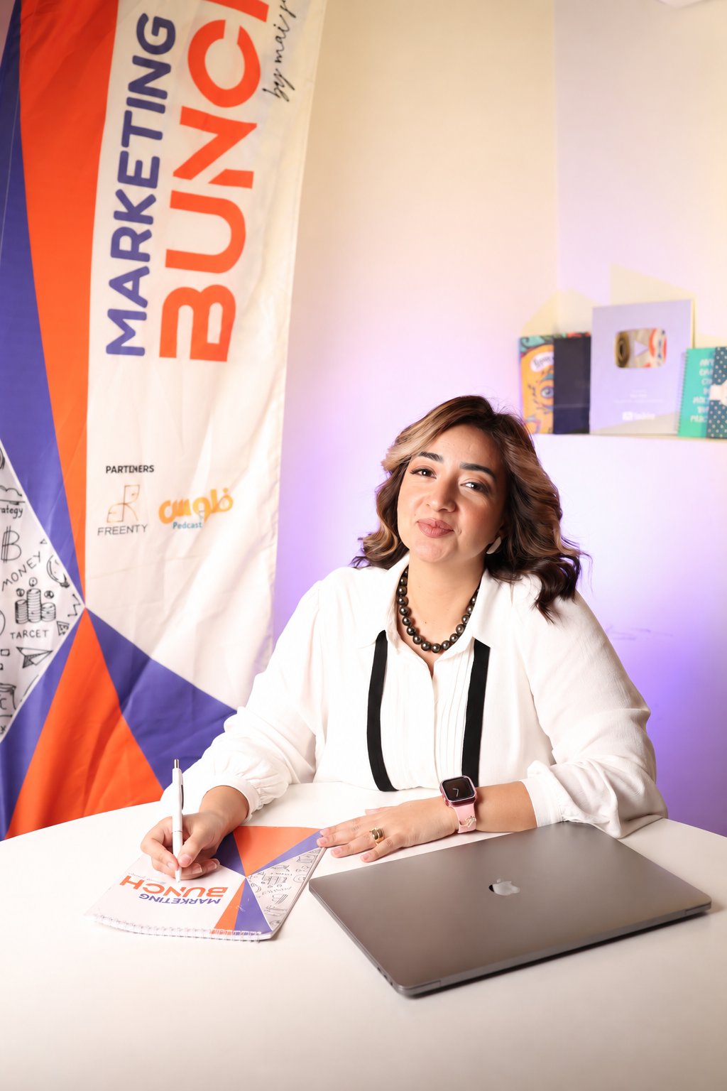Mai Sami seated at her desk writing, with her YouTube Silver Creator Award on the shelf behind her
