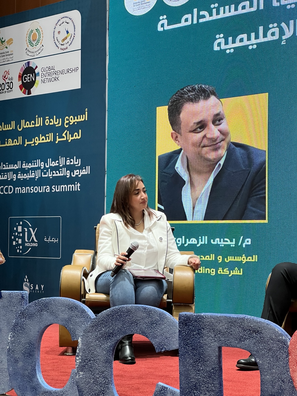 Mai Sami seated with her microphone and tablet while moderating the UCCD Mansoura Summit panel
