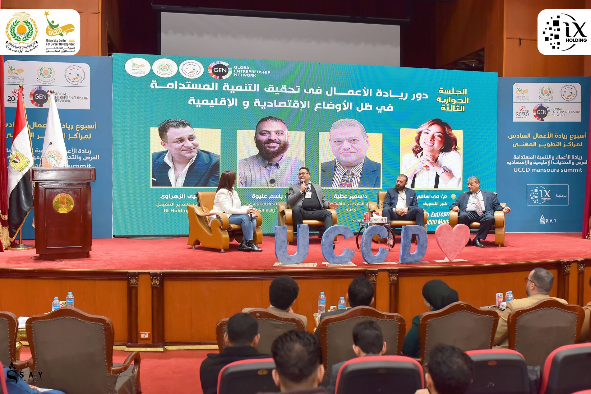 Wide photograph of Mai Sami moderating the seated panel at UCCD Mansoura Summit