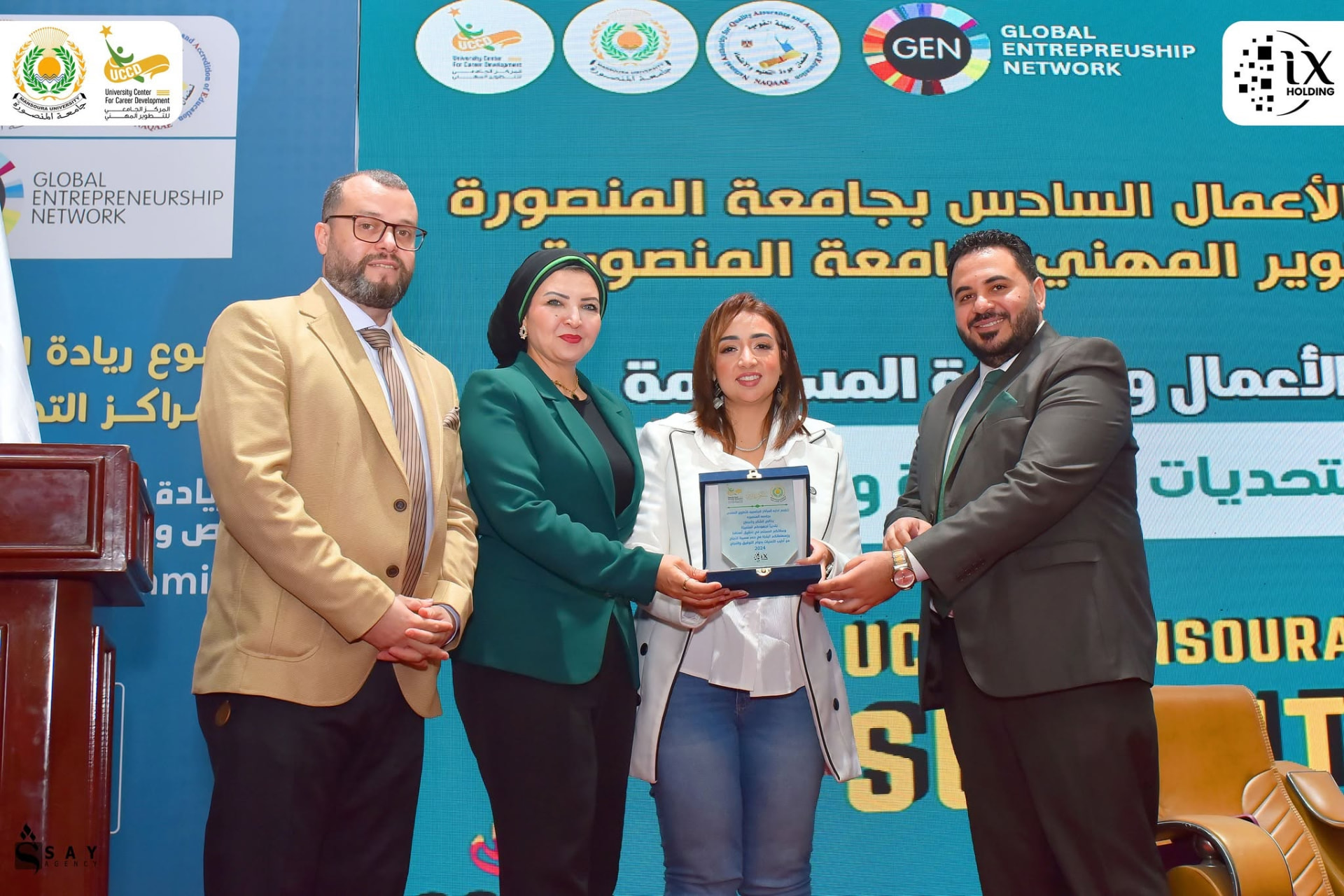 Mai Sami holding a recognition plaque with a group at UCCD Mansoura Summit