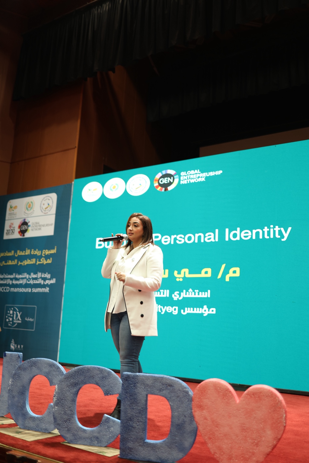 Mai Sami speaking into a microphone on stage during her personal branding talk at UCCD Mansoura Summit